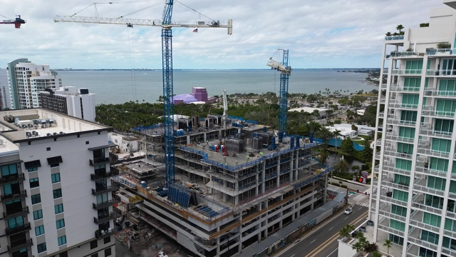 Aerial view of a waterfront high-rise construction site with cranes and surrounding buildings.