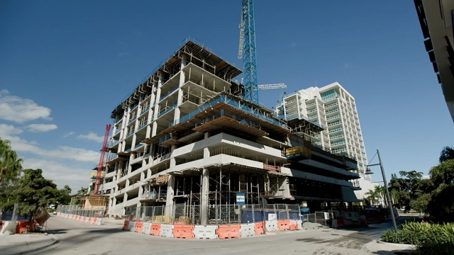 Ground-level view of a multi-story concrete structure under construction with cranes overhead.