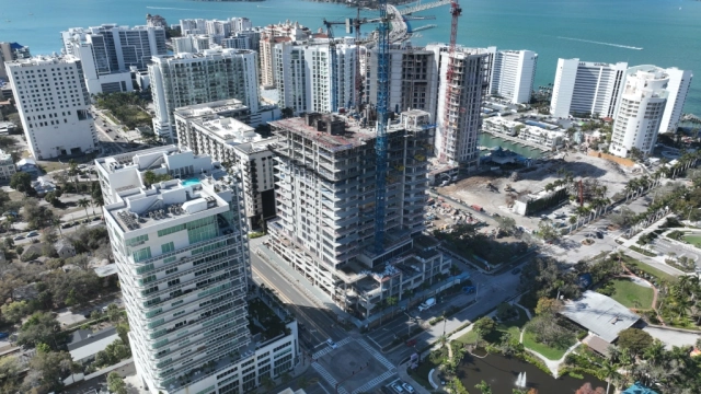 Southwest aerial of tower construction near bay and bridge.