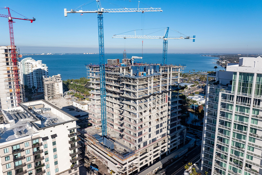 High-rise building under construction with tower cranes beside waterfront