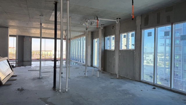 Unfinished high-rise interior with plumbing pipes and large windows.