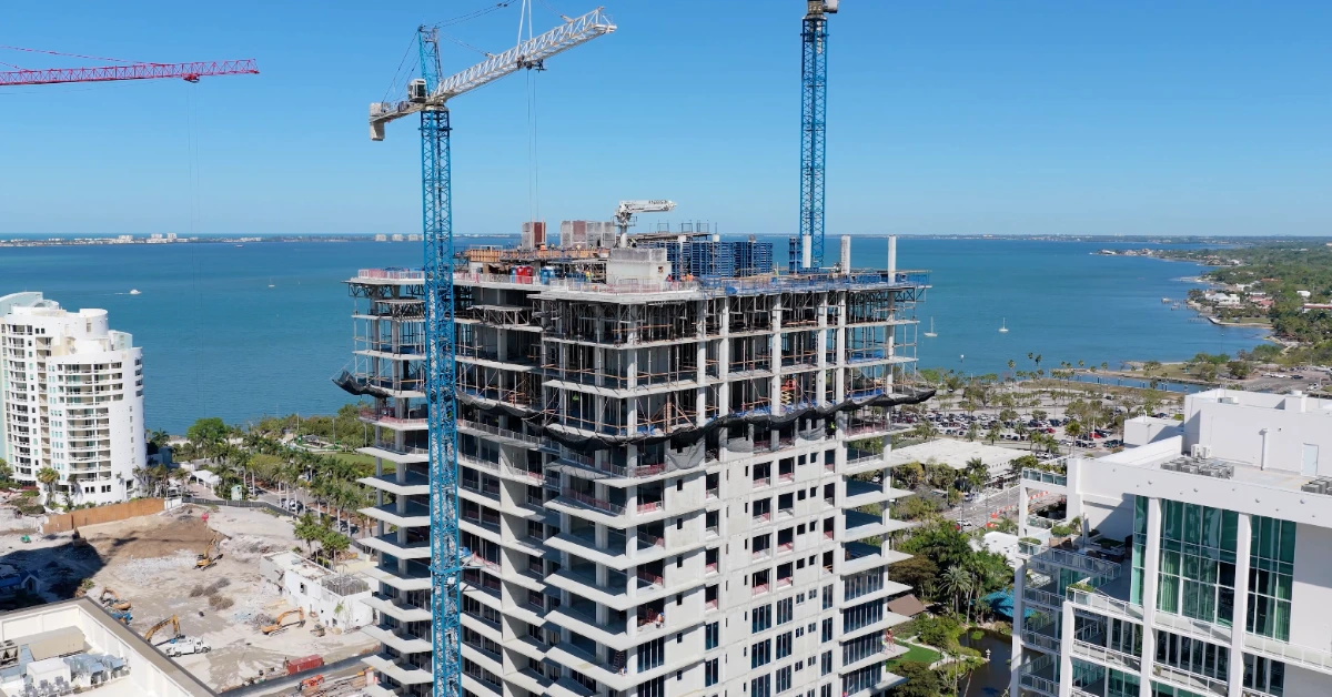 High-rise under construction with cranes overlooking waterfront and city skyline